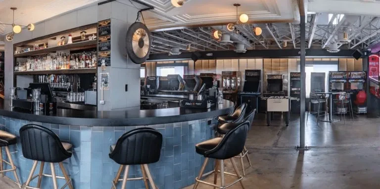 Modern, empty bar-arcade featuring a curved bar and arcade games.