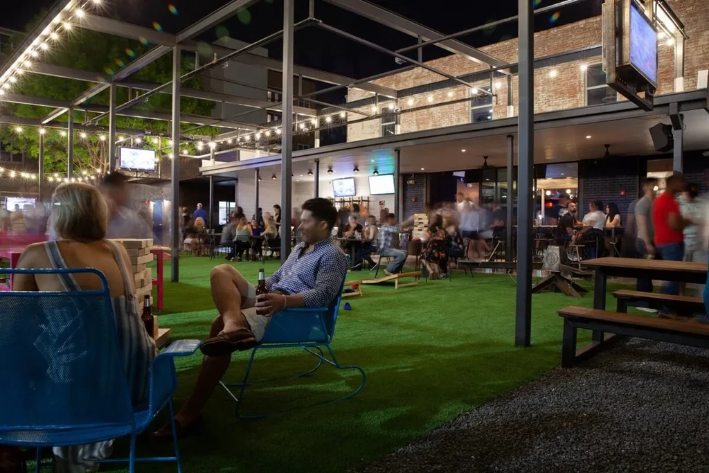 Nighttime outdoor patio with string lights, blurred patrons, some playing games.