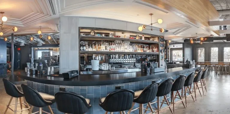 Modern bar interior with blue-tiled curved counter and liquor display.