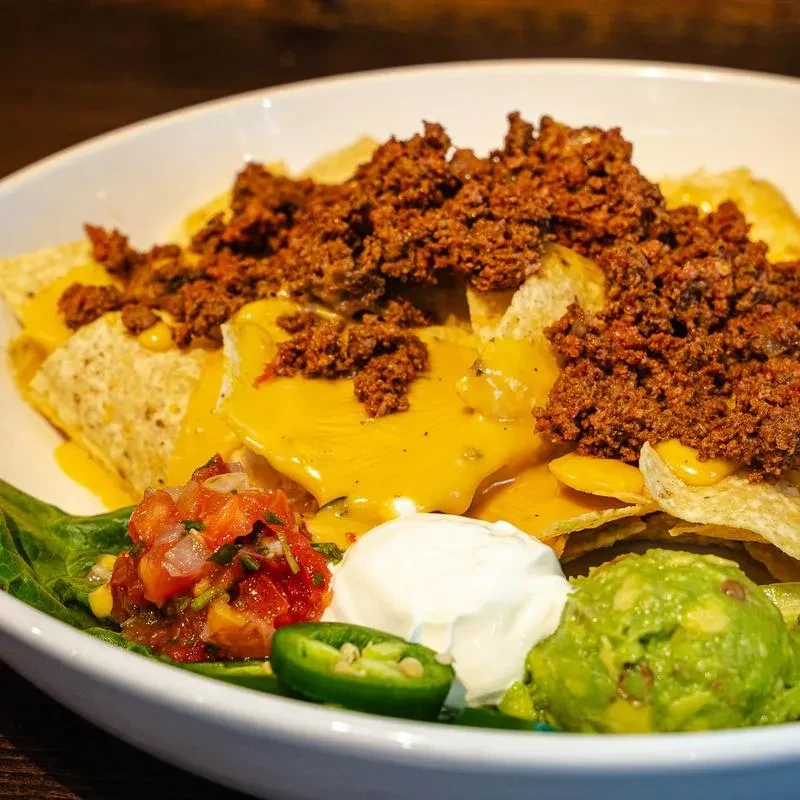Nachos with melted cheese, seasoned meat, salsa, guacamole, and sour cream.