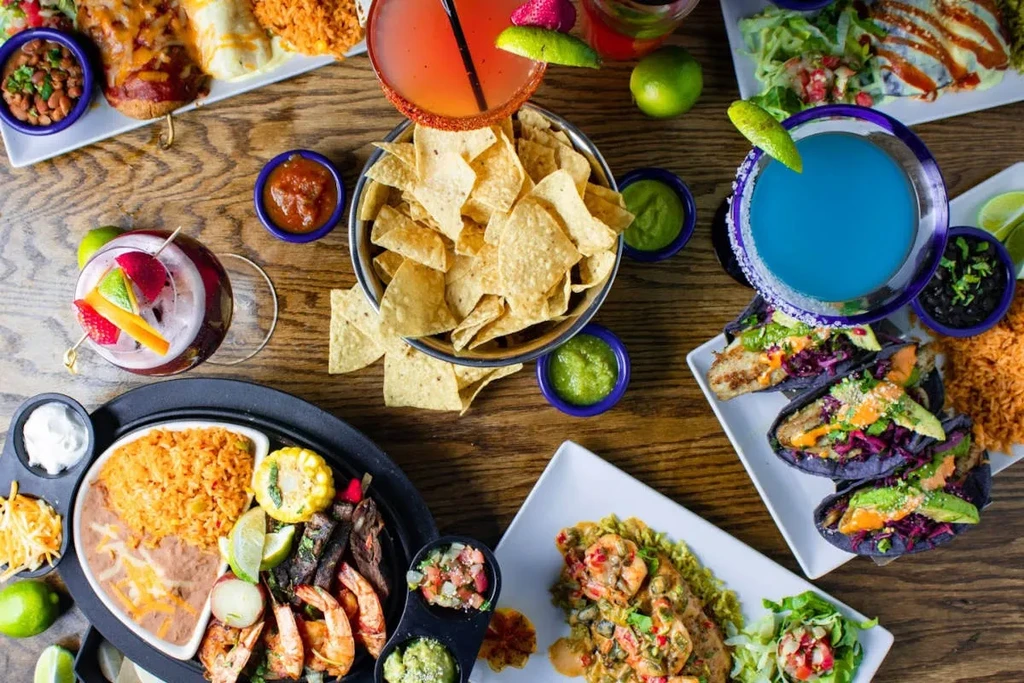 Overhead: Wooden table laden with colorful Mexican food and cocktails.