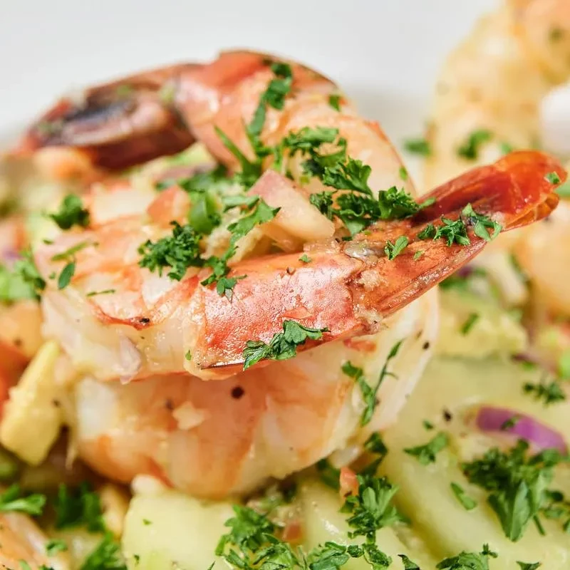 Close-up of cooked shrimp with fresh green herbs, mixed vegetables, and creamy dressing.