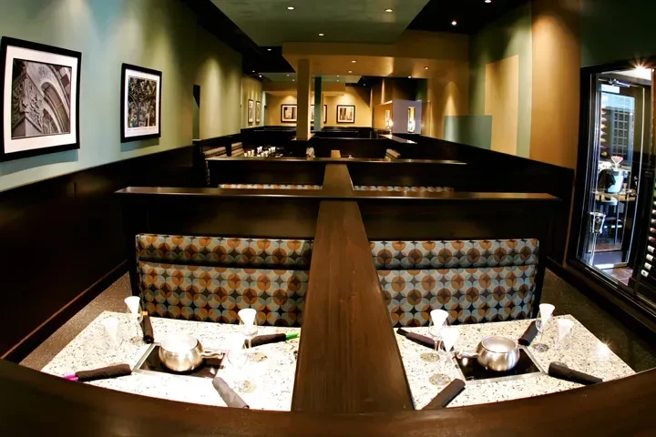 Restaurant dining room with booth seating, fondue pots, and patterned upholstery.