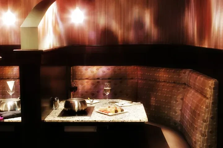 Restaurant booth with fondue, dessert, wine, under warm lighting.