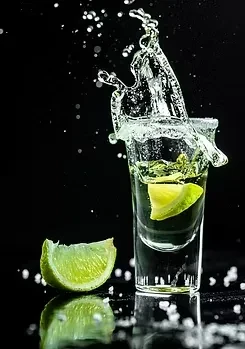 Splashing shot glass of yellow liquid with lime and salt.