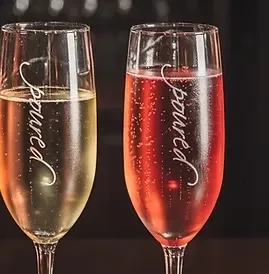 Two flutes with light and dark sparkling drinks, etched with 'poured'.
