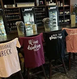 Four bar stools draped in wine-themed t-shirts at a Bubbly Bar.