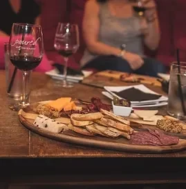 Close-up: Charcuterie board, wine, drinks on rustic table in cozy bar.