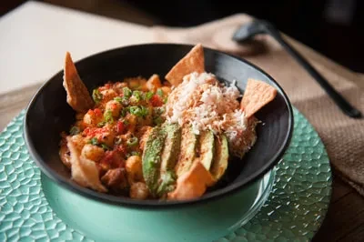 Colorful dish with chickpeas, avocado, and chips in a black bowl.