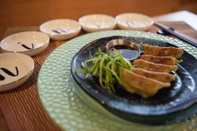 Gyoza, dipping sauce, and green onions on a restaurant table.