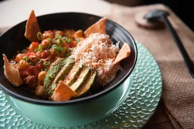 Meticulously arranged colorful dish with chickpeas, avocado, crab, and chips.