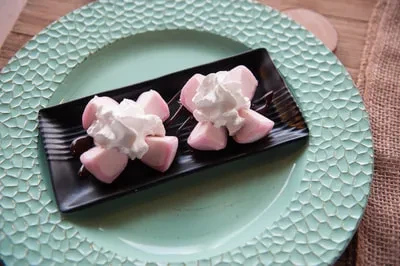 Two pink petal desserts with whipped cream on a textured teal plate.