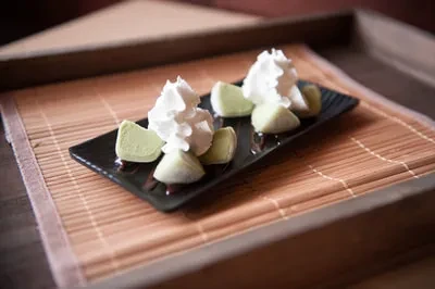 Two light green confections, whipped cream, dark sauce, black plate.