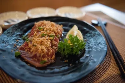Sashimi/carpaccio with golden crumbs, green onions, lemon, and black chopsticks.