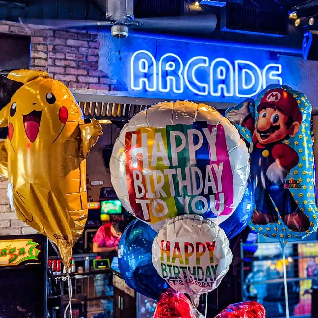 Pikachu, Mario, and Birthday balloons in a vibrant arcade with a neon sign.