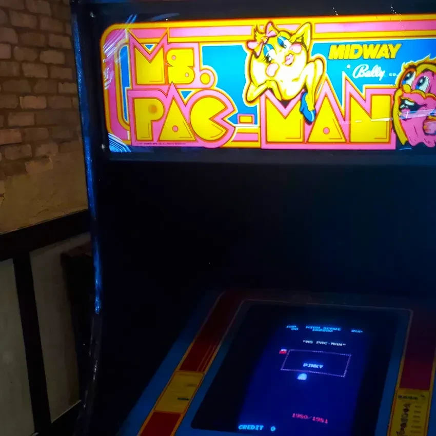 Illuminated Ms. Pac-Man arcade cabinet with glowing screen and marquee.