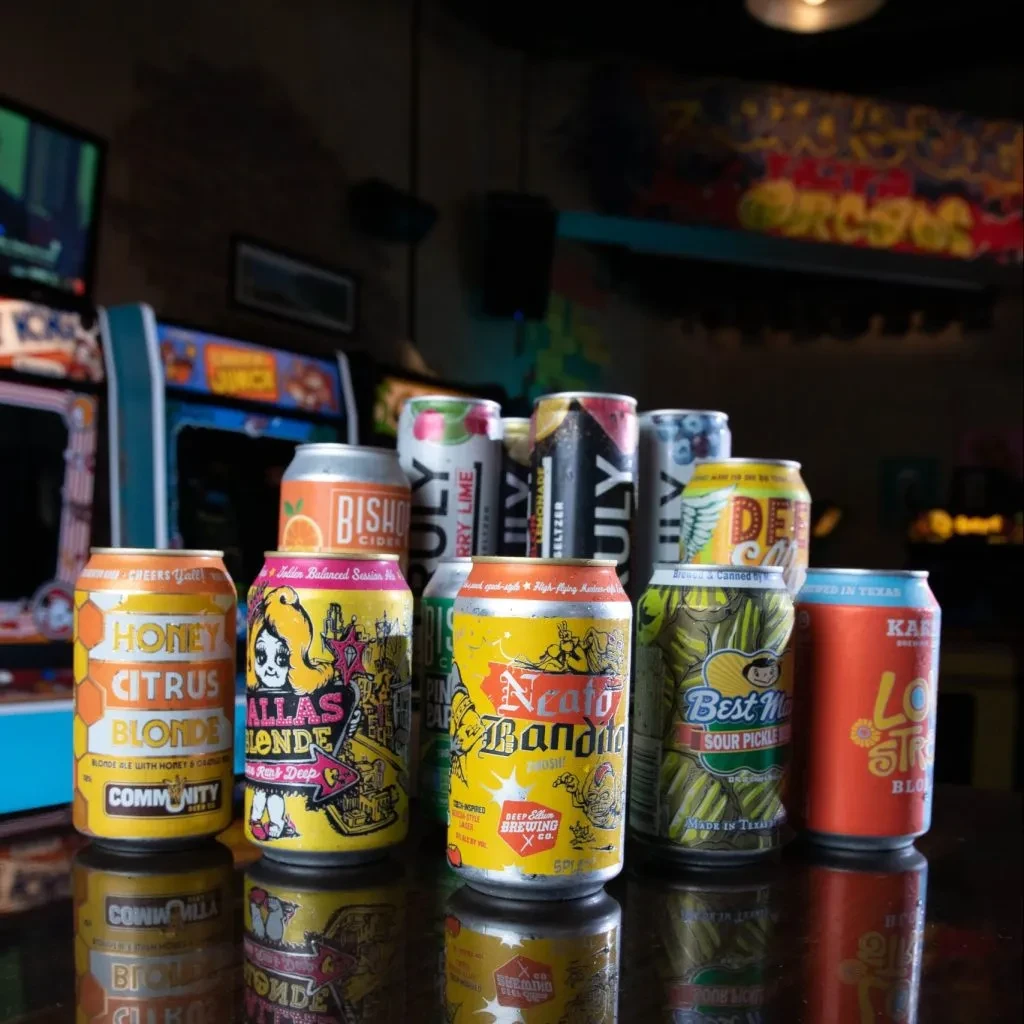 Cold, colorful craft cans on a reflective bar counter in an arcade.