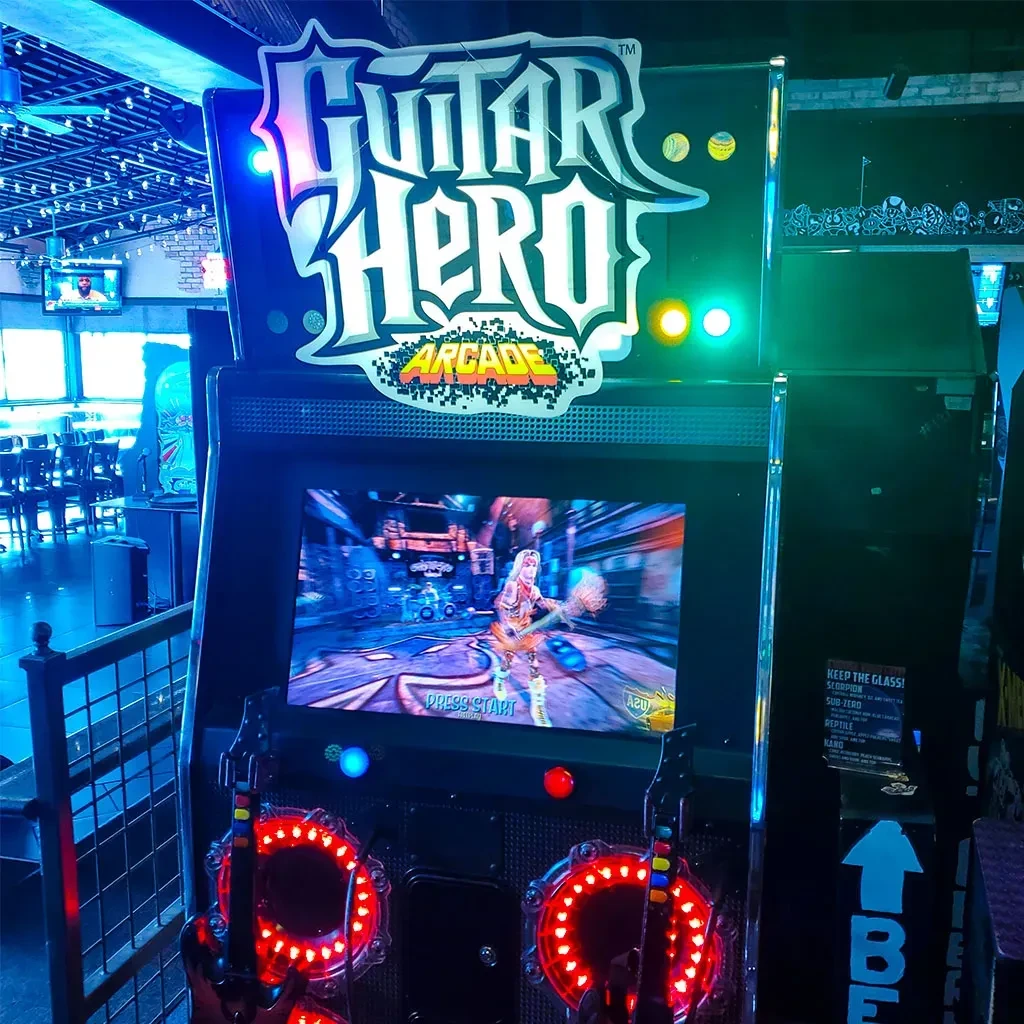 Guitar Hero arcade machine in a blue-lit restaurant with glowing controllers.