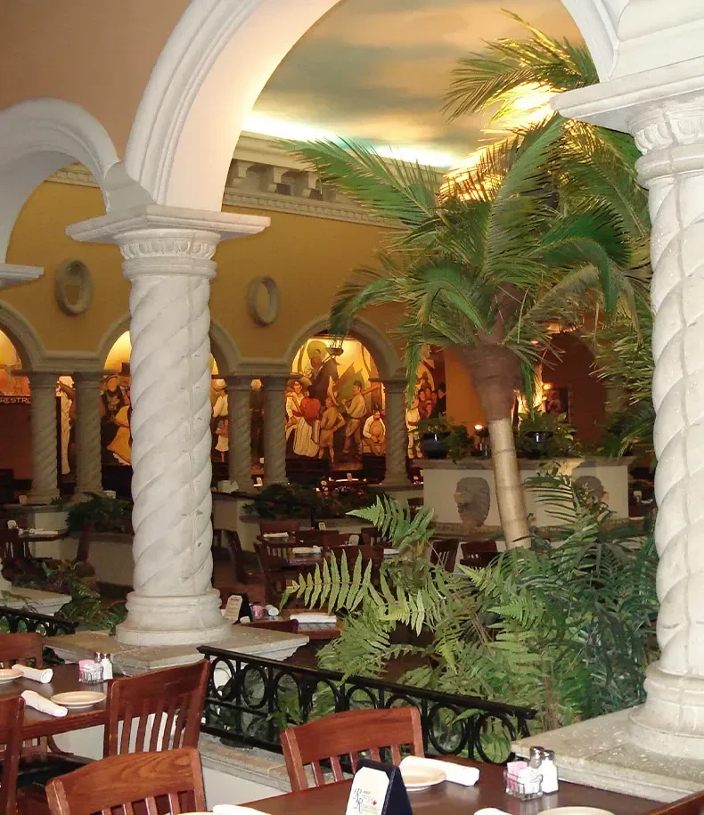 Ornate restaurant interior with spiraled columns, sky ceiling, plants, and set tables.