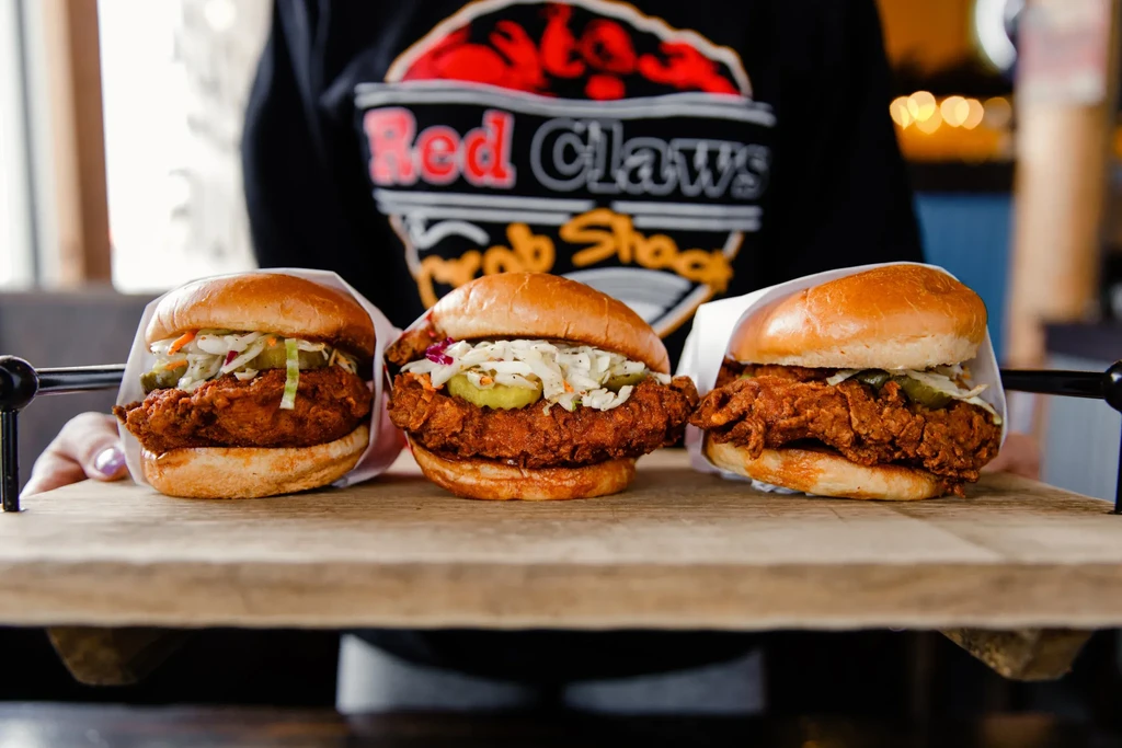 Three crispy fried chicken sandwiches with coleslaw and pickles on a board.