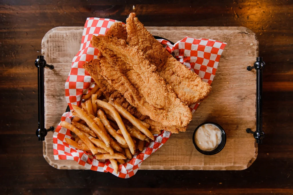 Fried fish and fries with dipping sauce served on a wooden board.