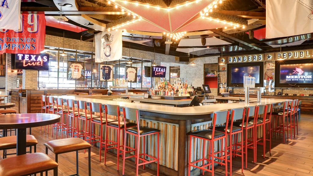 Vibrant sports bar interior with a large bar, red stools, and TVs.