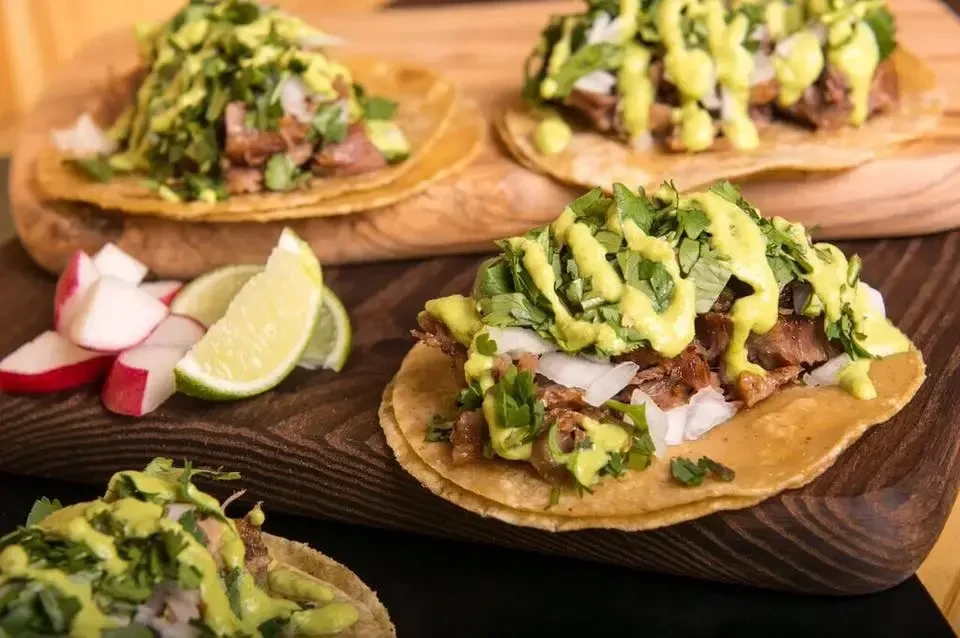 Four meat tacos with onions, cilantro, green sauce, lime on wood.