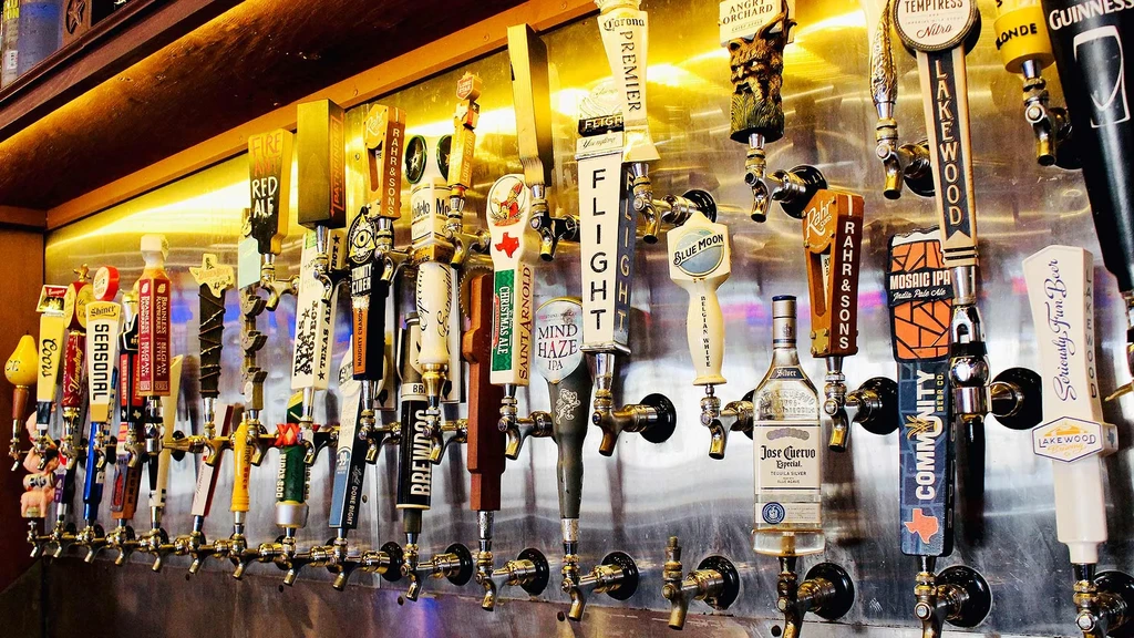 Many beer taps and liquor dispensers on a reflective bar wall.
