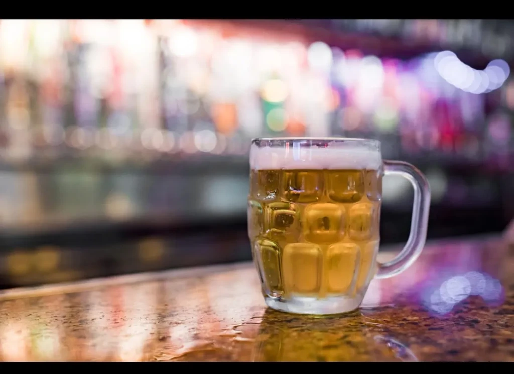 Golden beer mug with frothy head on wet bar, blurred background.