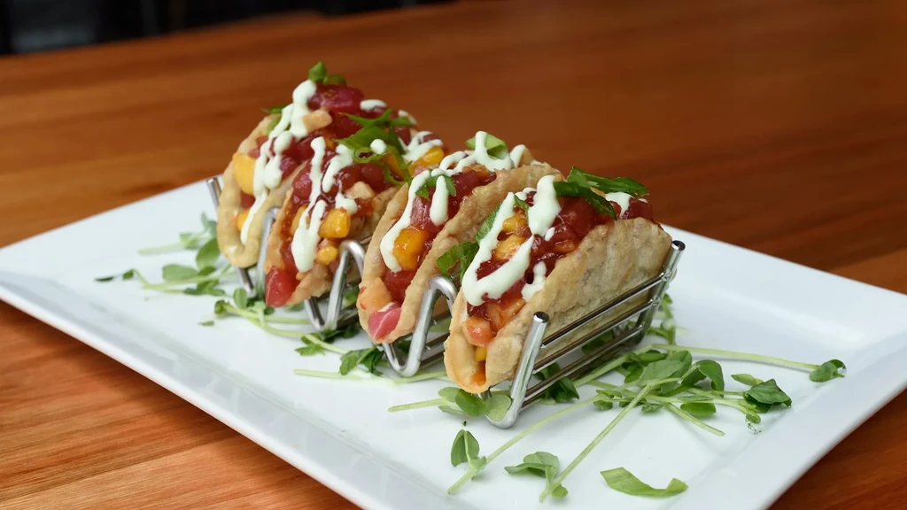 Four tacos with red filling, golden pieces, creamy green sauce, herbs.