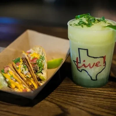 Three street tacos, frozen lime drink in Texas-logo cup on wood.