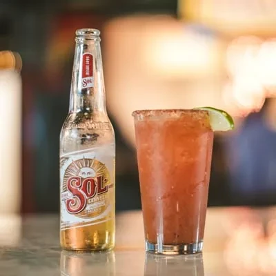 Cold Sol beer bottle and chili-lime cocktail on a bar.