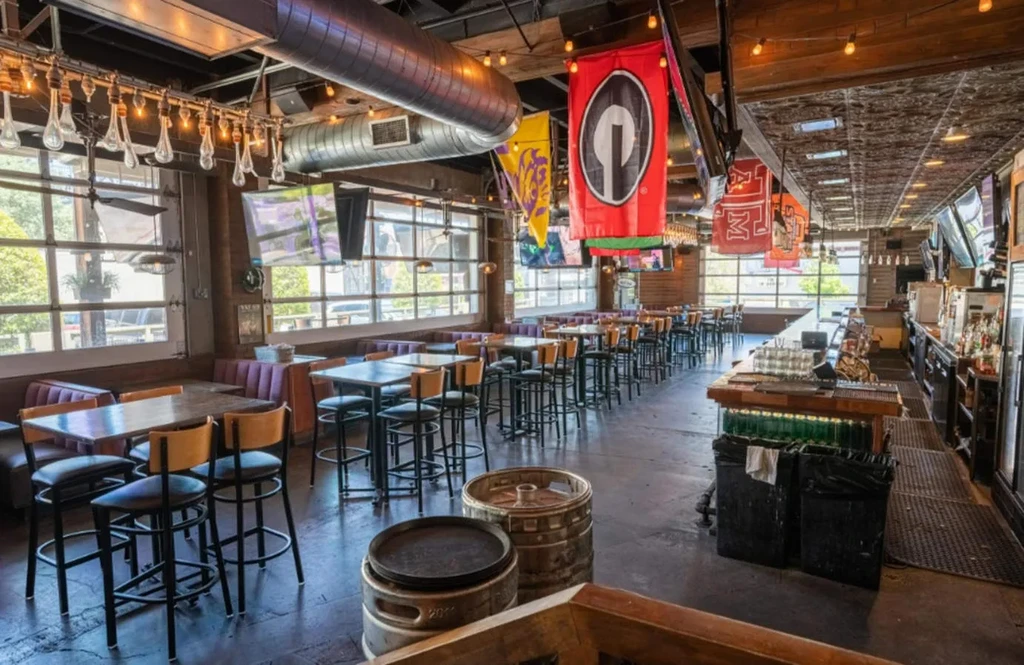 Modern sports bar with empty dining area, bar, and sports decor.
