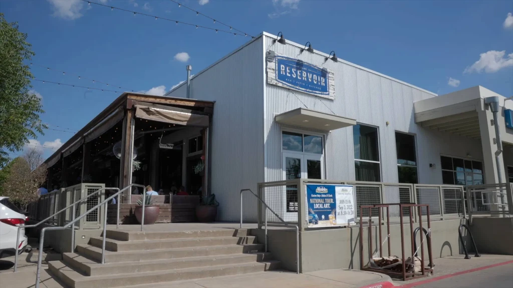Reservoir restaurant exterior: modern corrugated building, sunny patio with people.