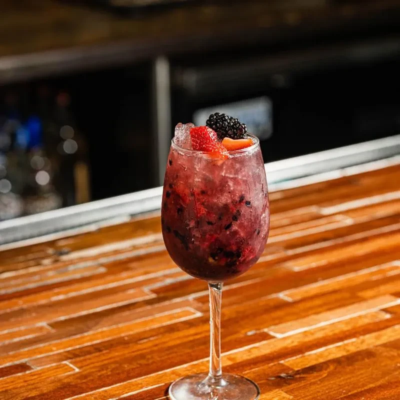 Red-purple berry cocktail with crushed ice, garnished with strawberries and blackberries.