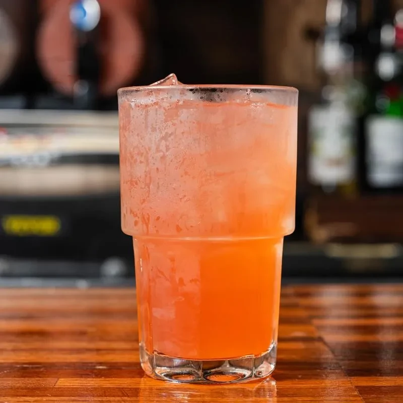 Heavily condensed glass with orange drink and ice on a bar.