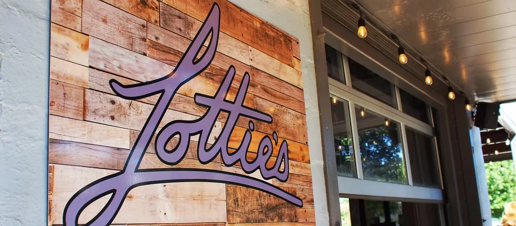 Stylized 'Lottie's' sign on a rustic wood wall with string lights.