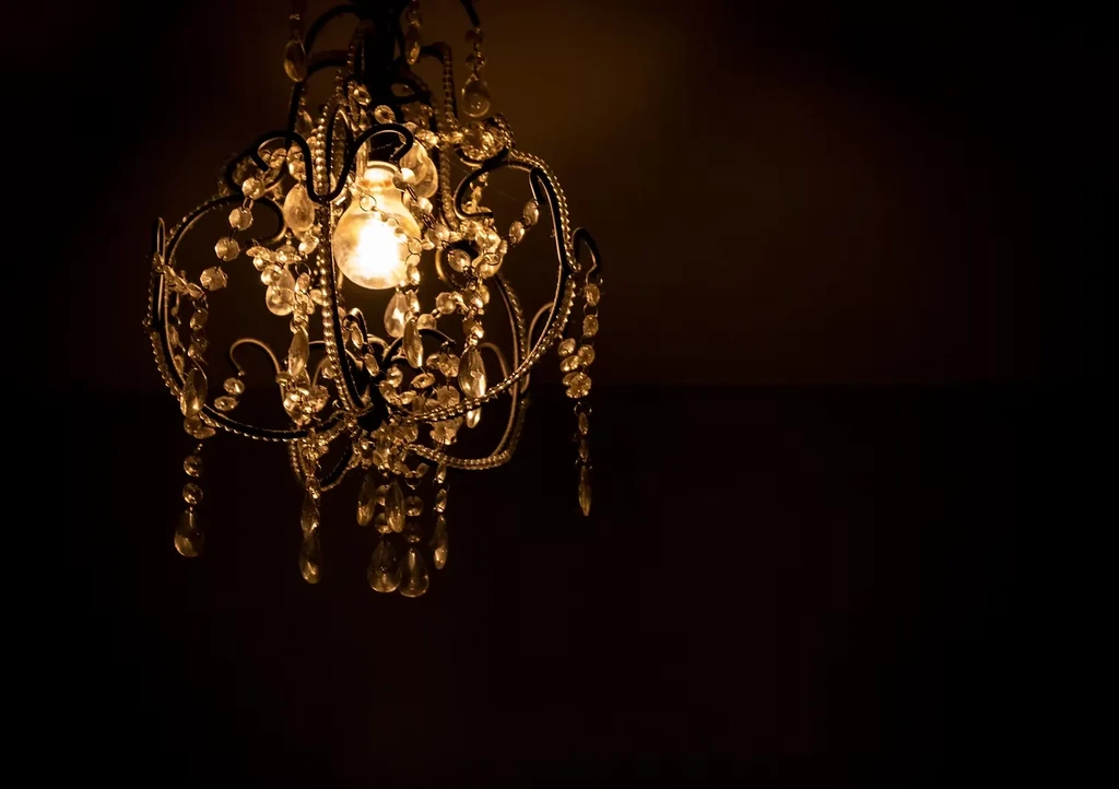 Ornate dark metal chandelier with glowing bulb and sparkling crystal details.