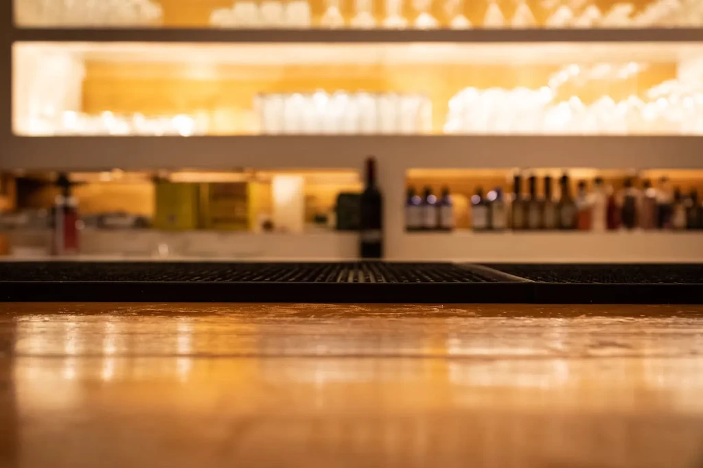 Warm-lit polished wooden bar counter with blurred bottles and glassware.