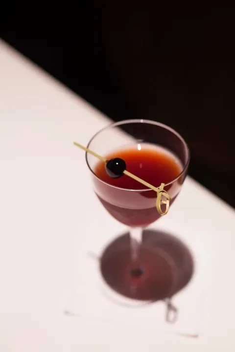 Close-up, high-angle dark cocktail with cherry in coupe glass.