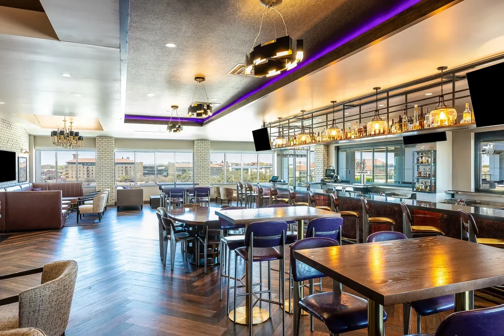 Empty modern restaurant interior with a bar, diverse seating, and purple lighting.