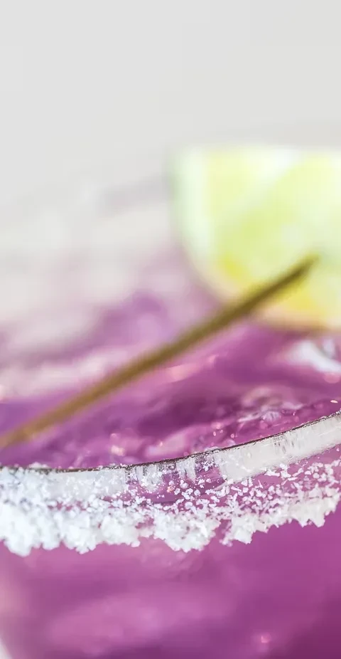 Purple cocktail with a white crystal-coated rim and lime.