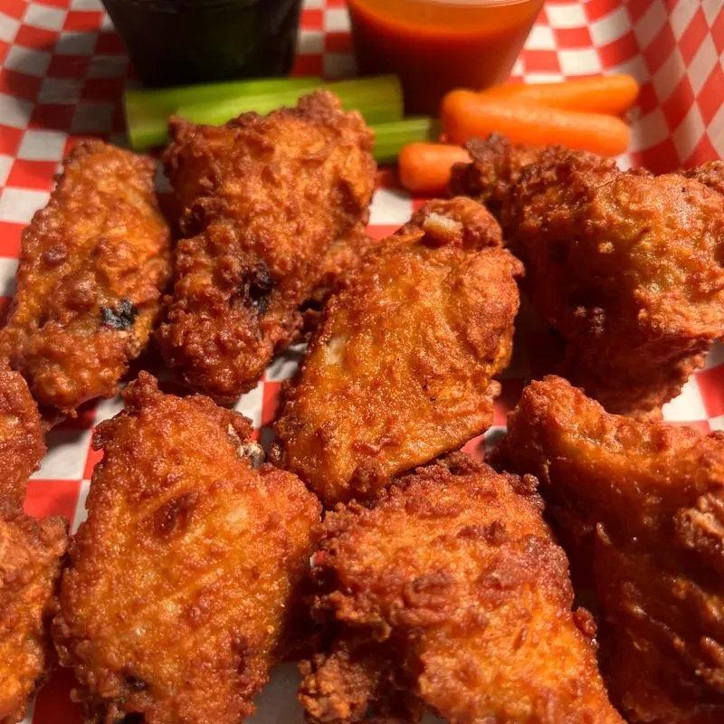 Crispy fried chicken wings on checkered paper with sauces, celery, and carrots.
