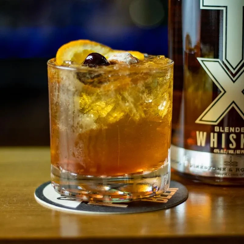 Amber cocktail in rocks glass with orange and cherry garnish.