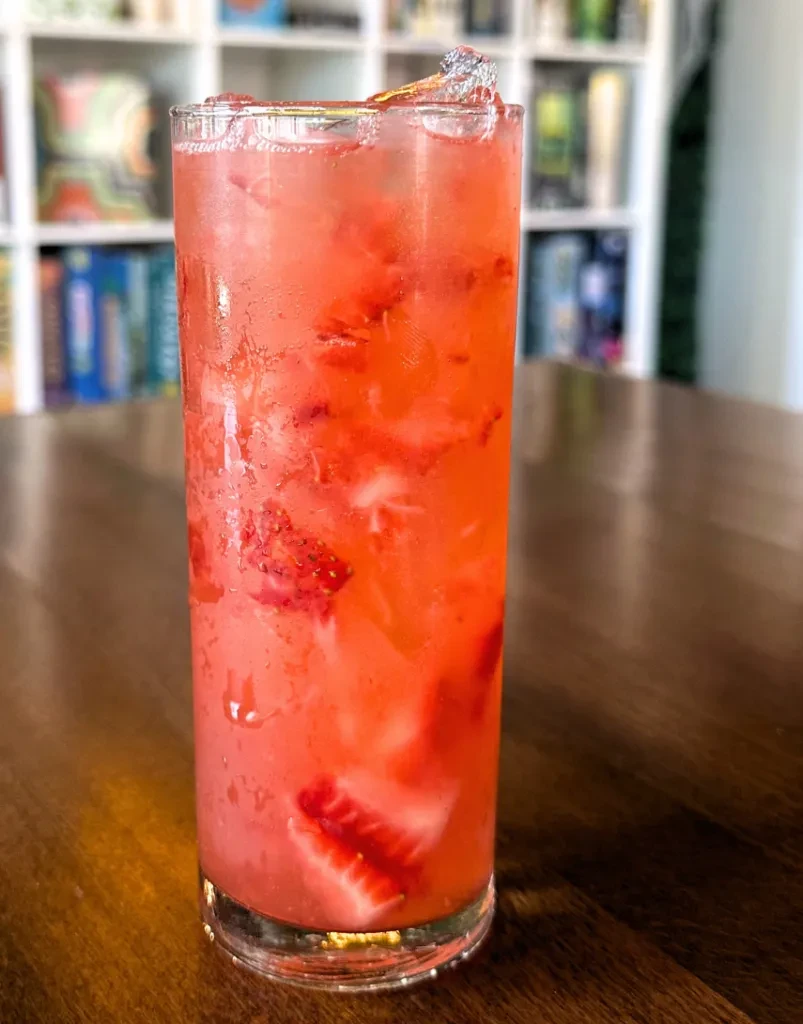 Glass of cold strawberry drink with ice and condensation on wood.