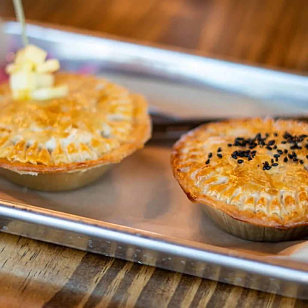 Two golden-brown pies on a tray, one with cubes, one with seeds.