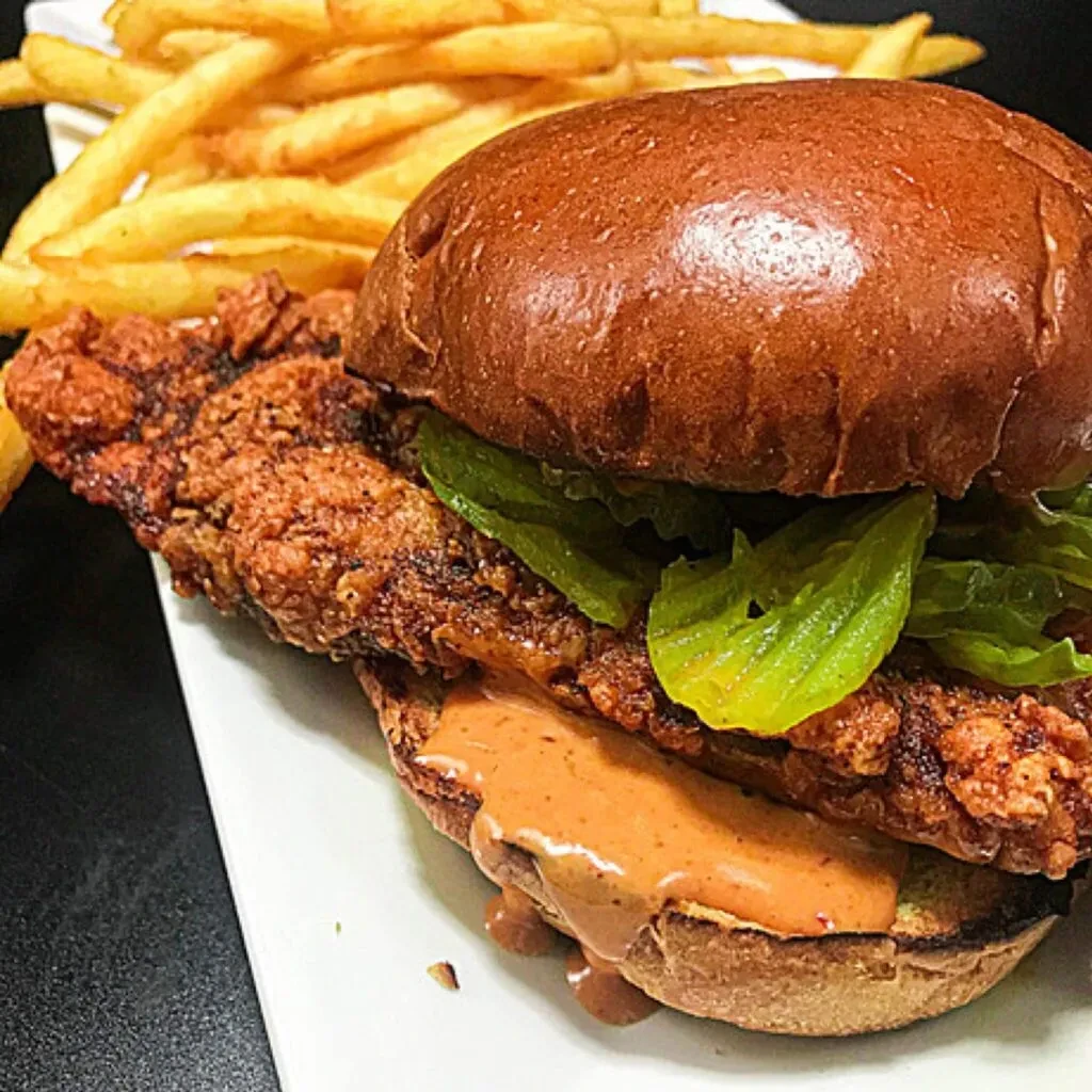 Crispy fried chicken sandwich with lettuce, sauce, and golden fries.