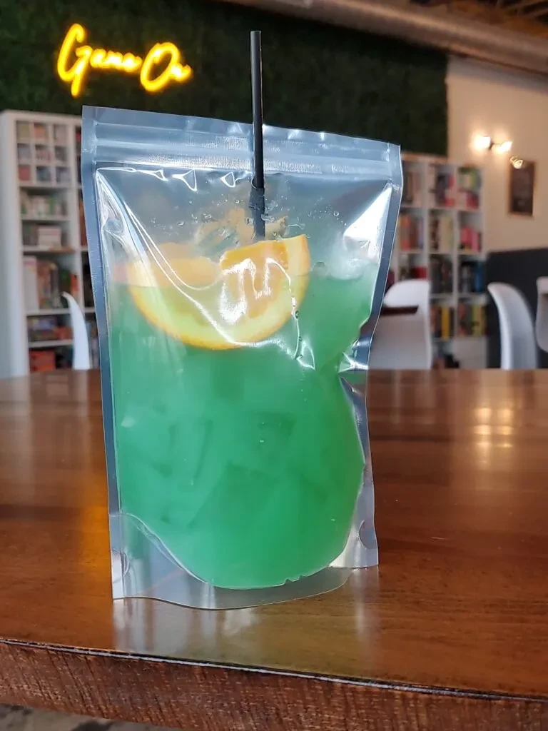 Green drink pouch with ice, orange, straw, 'Game On' sign.