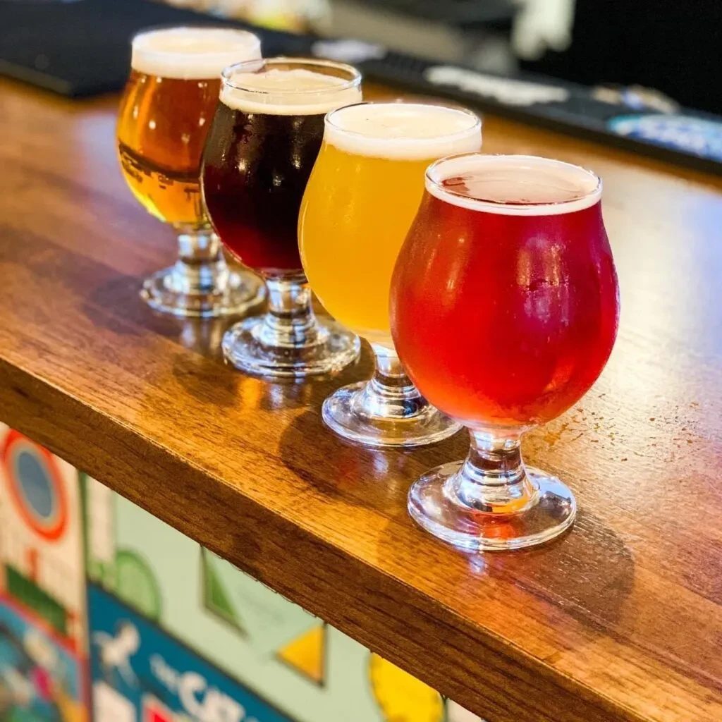 Flight of four cold, colorful beverages on a wooden bar.