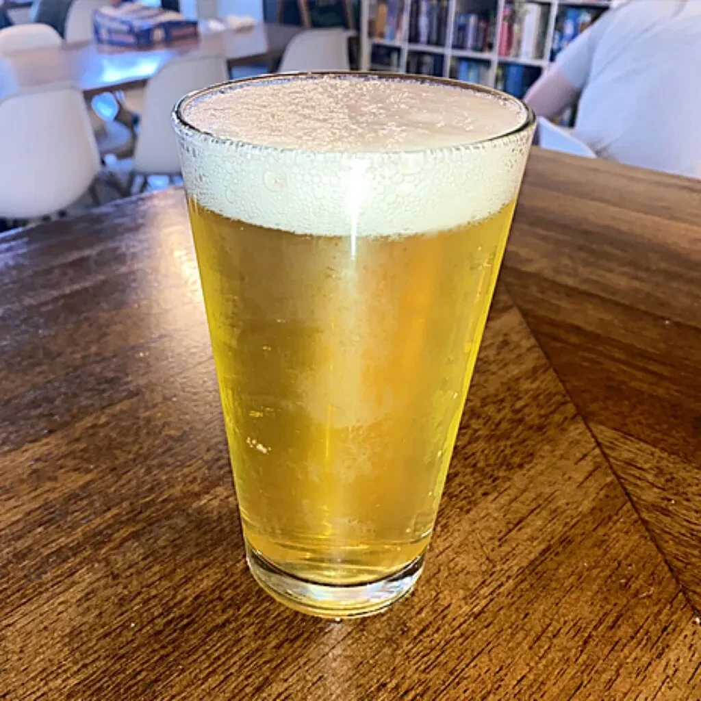 Cold pint of frothy golden beer on a dark wooden table.